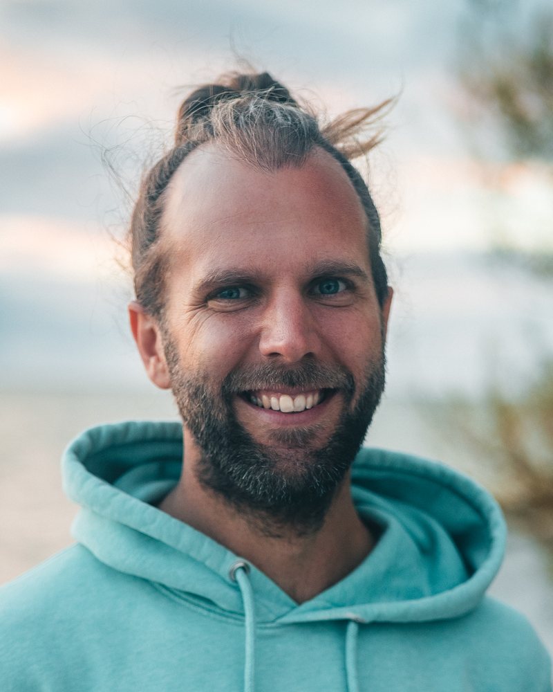 Dominik Kramer lacht in die Kamera, im Hintergrund das Wasser